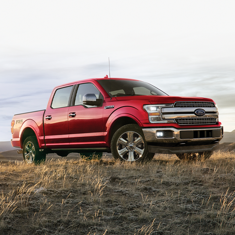 side view of red Ford F-150 on a dirt terrain with mountains in the background