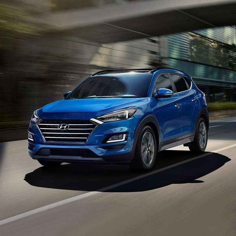 side profile view of blue hyundai tucson suv accelerating through the city streets