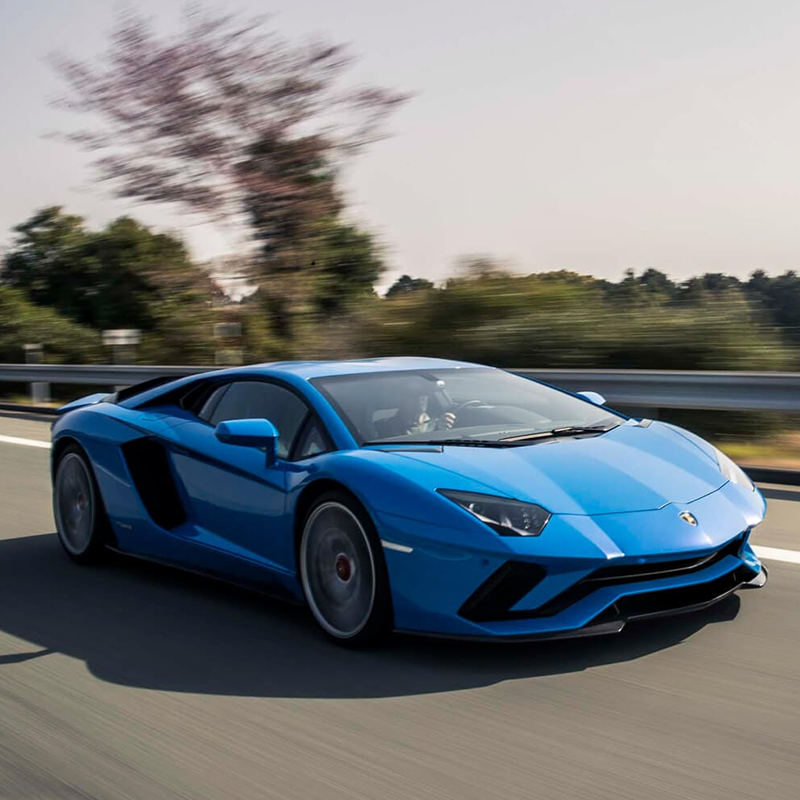 frontal profile of blue lamborghini huracan aventador on a road with trees around