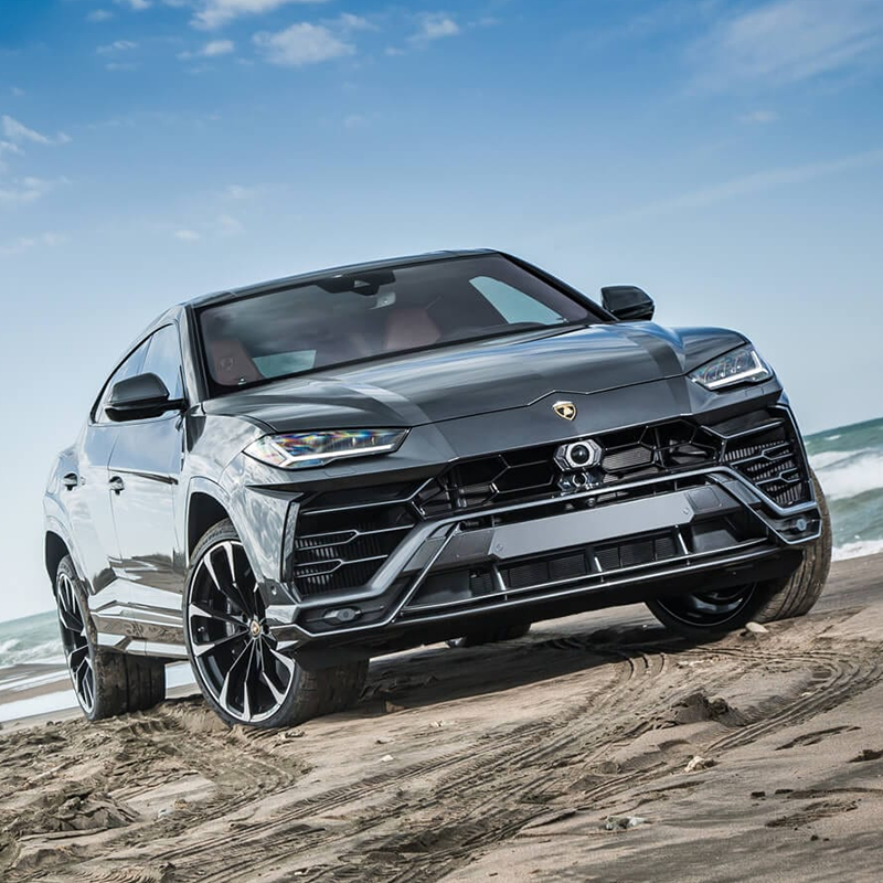 gray Lamborghini urus suv parked on sand with a beach in the background