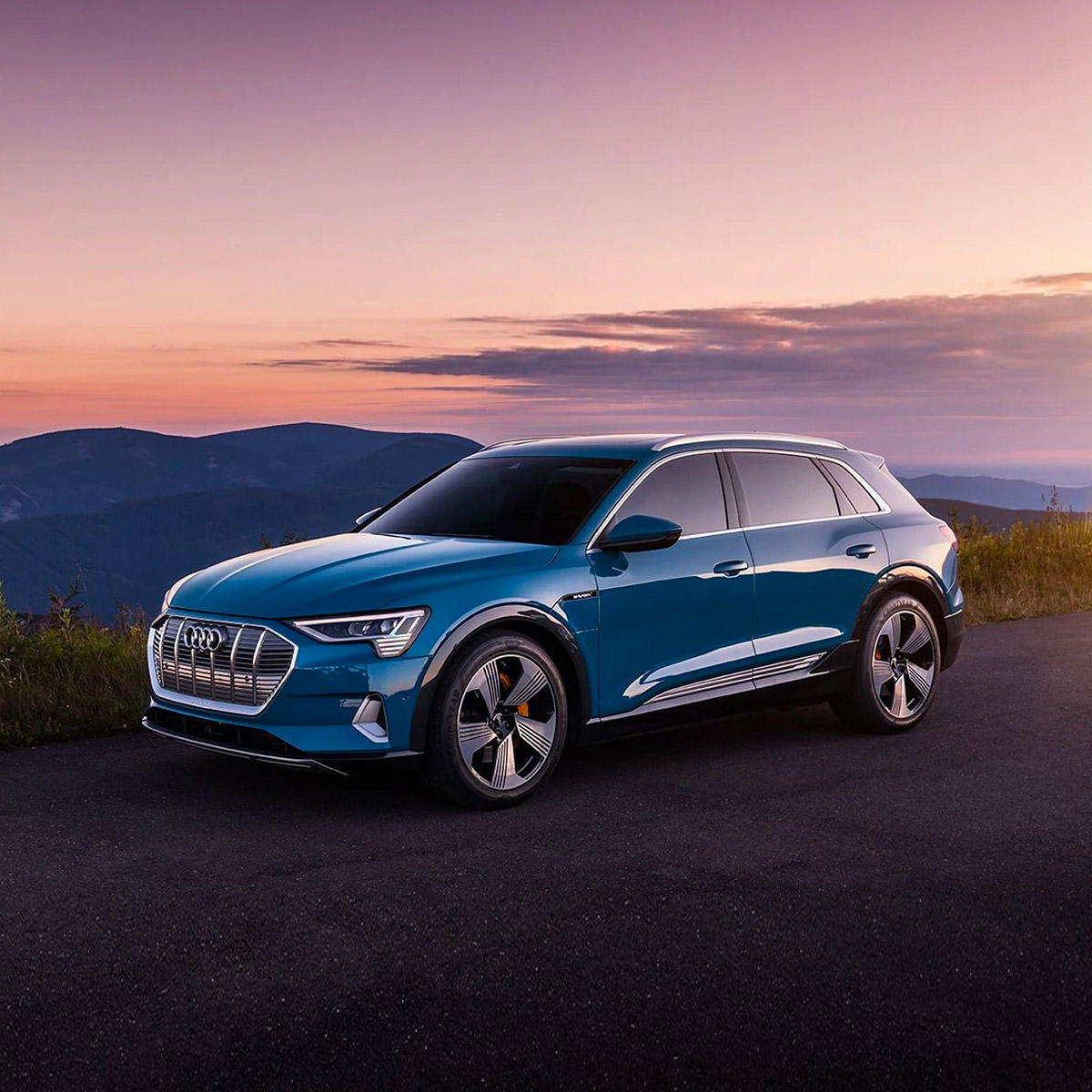 side profile of audi E-tron electric suv in blue color parked on pavement with mountains in the horizon at sunset