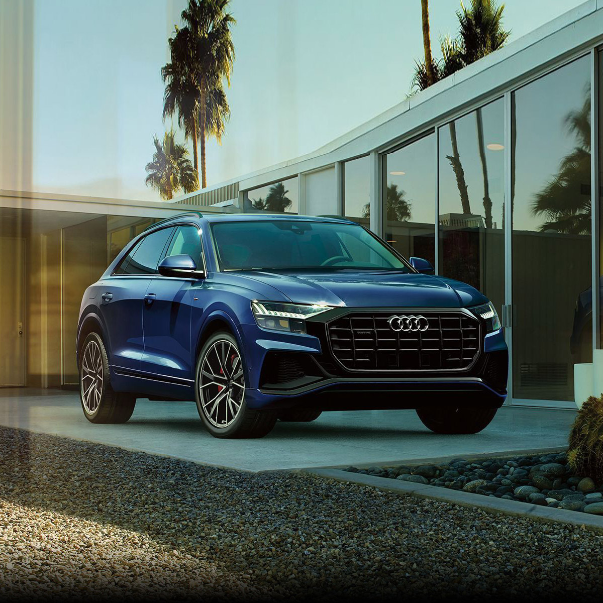 frontal profile of audi Q8 suv in blue color parked in a house driveway with palm trees in the background