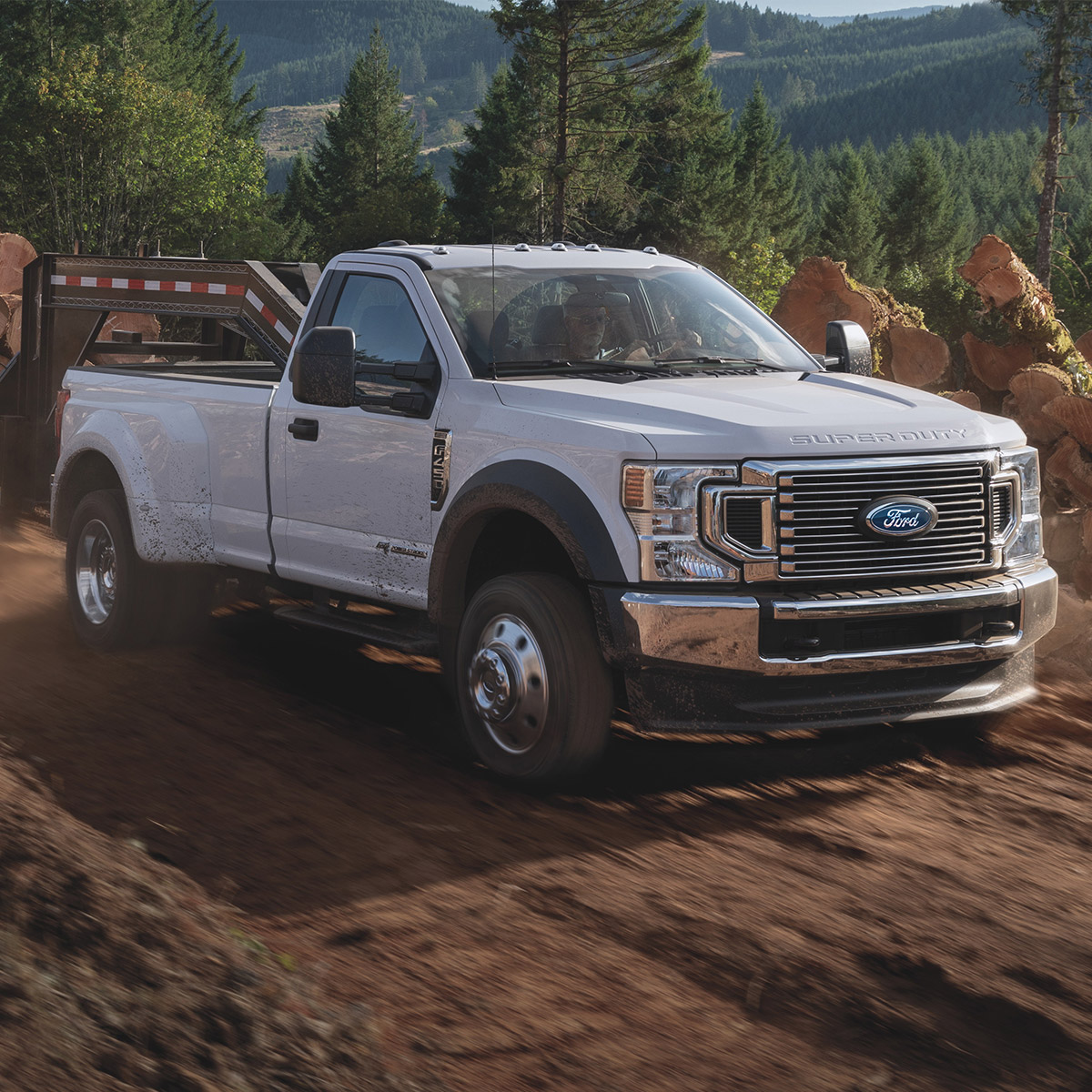 side profile of ford superduty pick up truck in white color driving on dirty terrain and mud surrounded by green muntains